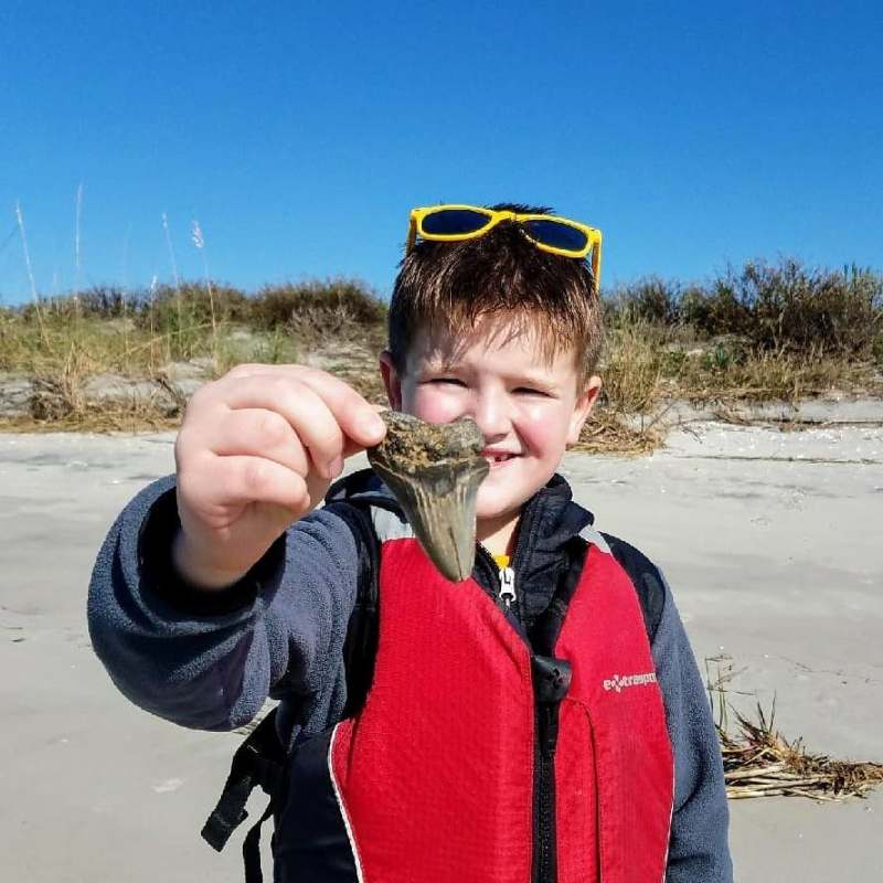 a boy wearing a hat and sunglasses posing near a body of water